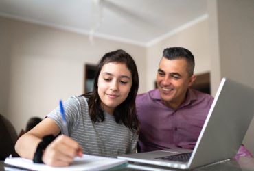 Father helping daughter studying using laptop at home