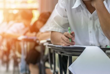 Exam at school with student's taking educational admission test in class, thinking hard, writing answer in university classroom, education and world literacy day concept