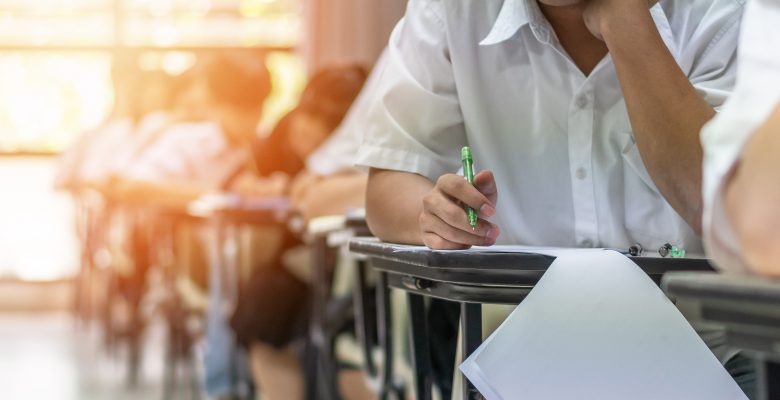 Exam at school with student's taking educational admission test in class, thinking hard, writing answer in university classroom, education and world literacy day concept